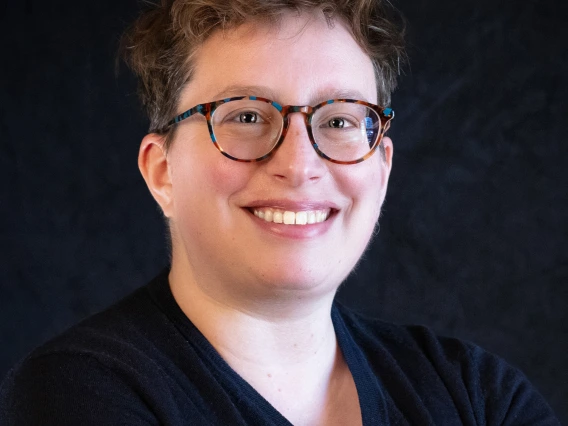 Woman with short hair and speckled glasses in a dark sweater.