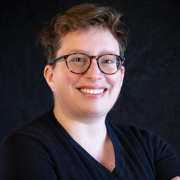 Woman with short hair and speckled glasses in a dark sweater.